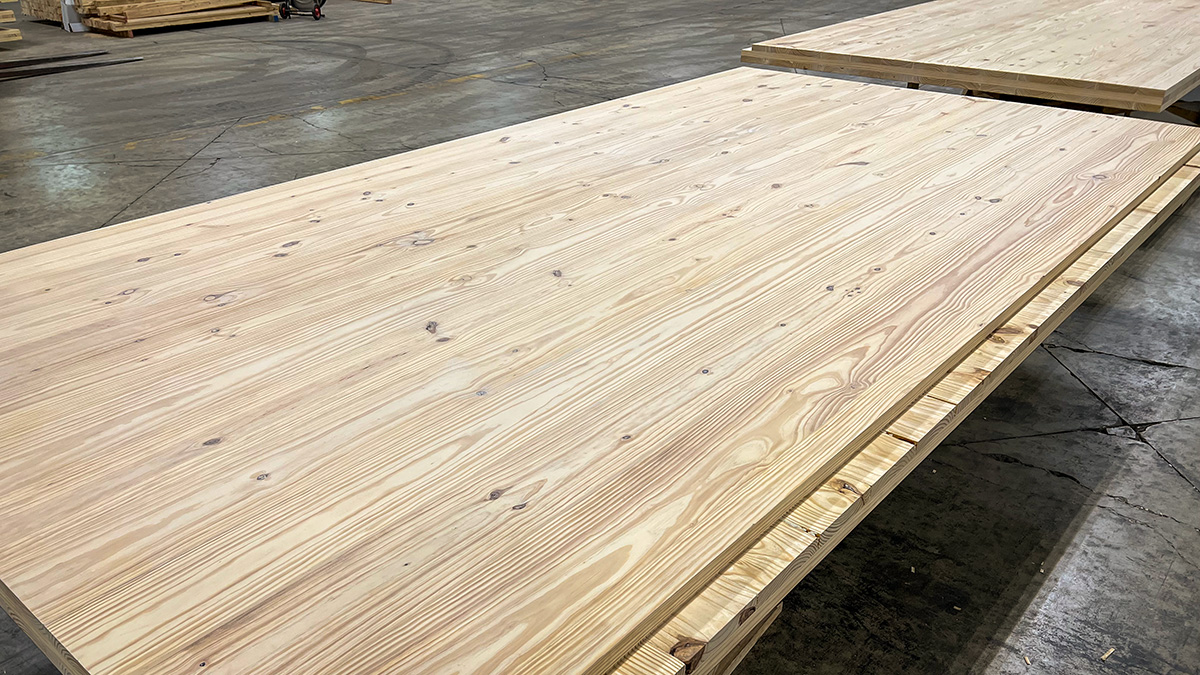 The image shows large wooden panels with smooth surfaces, neatly stacked on the floor of an industrial space. The wood grain is clearly visible, showcasing the natural texture and patterns of the timber.