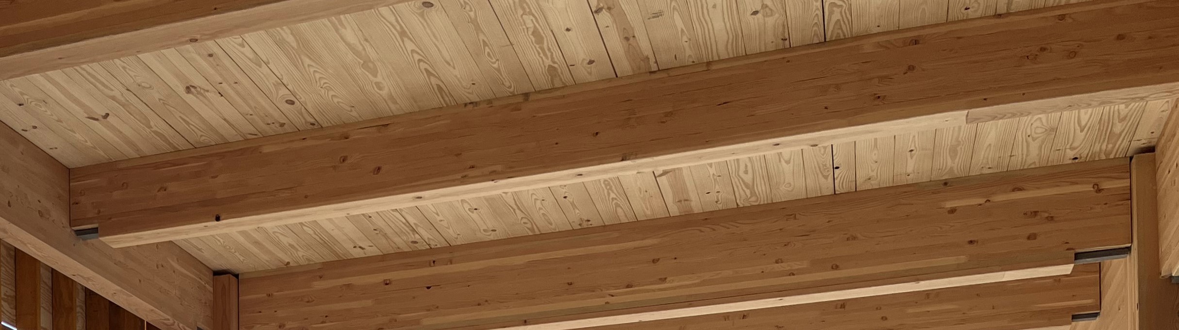 A close-up view of wooden glulam beams and a mass timber ceiling in a building under construction, showcasing natural wood grain and textures.