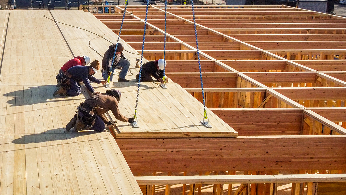 Workers secure mass timber panels onto a building frame with crane assistance.