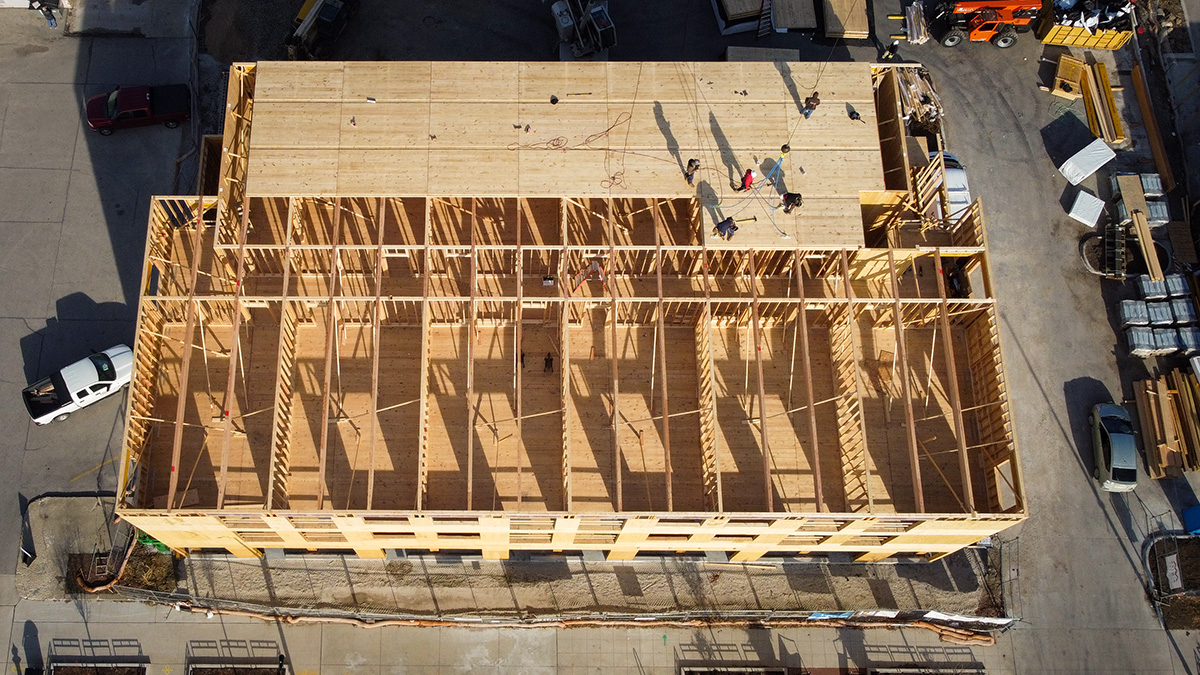 Overhead view of a building under construction with wooden framework and CLT panels, workers visible on-site.