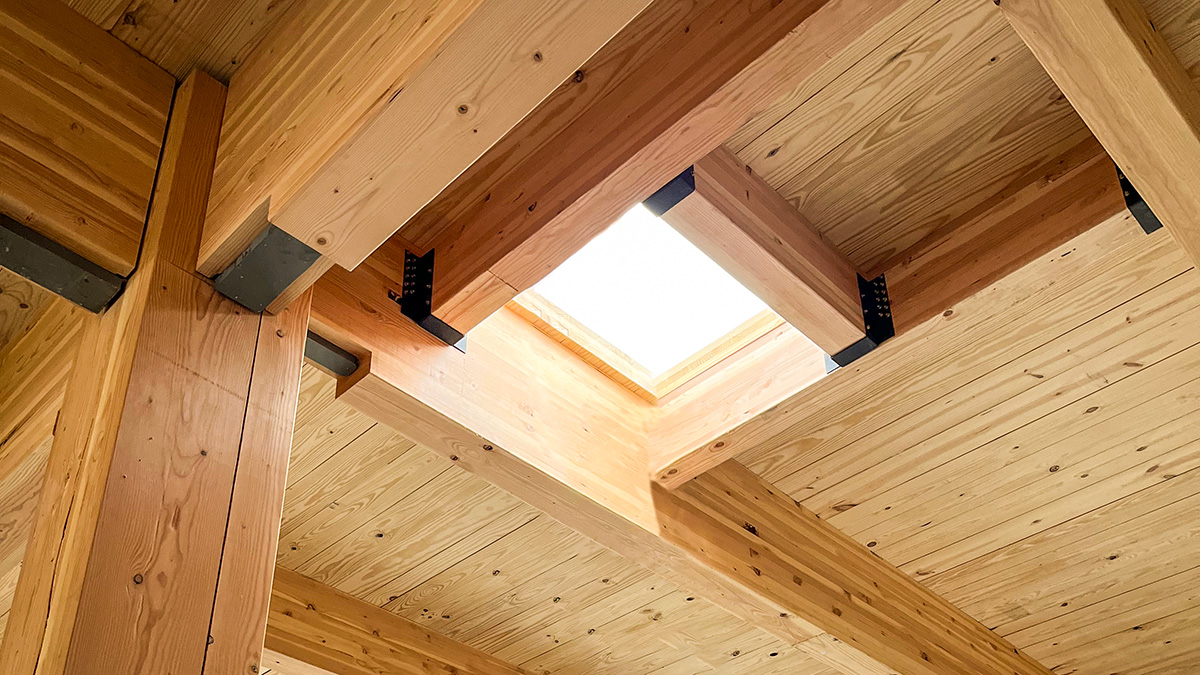 A rectangular opening in the mass timber ceiling of a wooden structure under construction, with beams and planks visible.