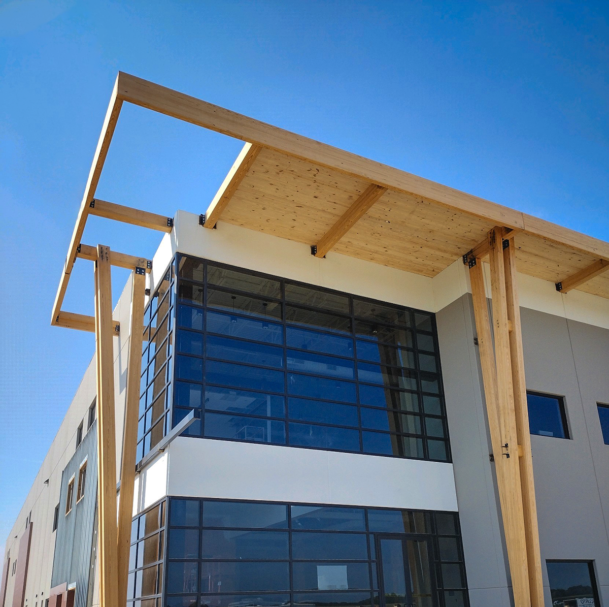 A modern building facade with exposed wooden beams and a CLT roof, featuring glass windows and gray panels.