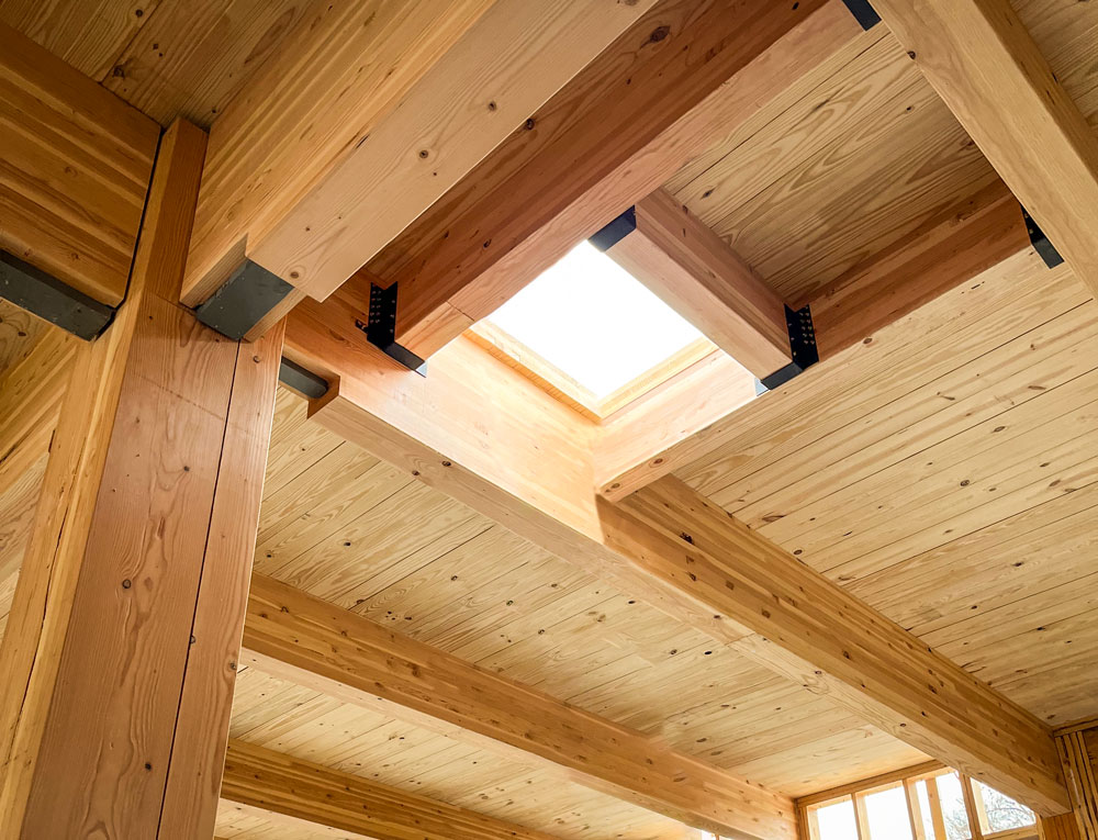 A rectangular opening in the mass timber ceiling of a wooden structure under construction, with beams and planks visible.