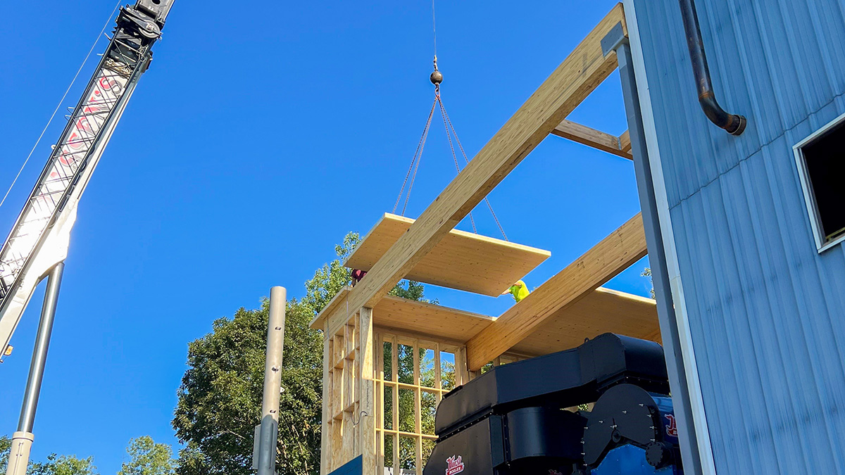 A construction scene of CLT panels being lifted by a crane against a clear blue sky.