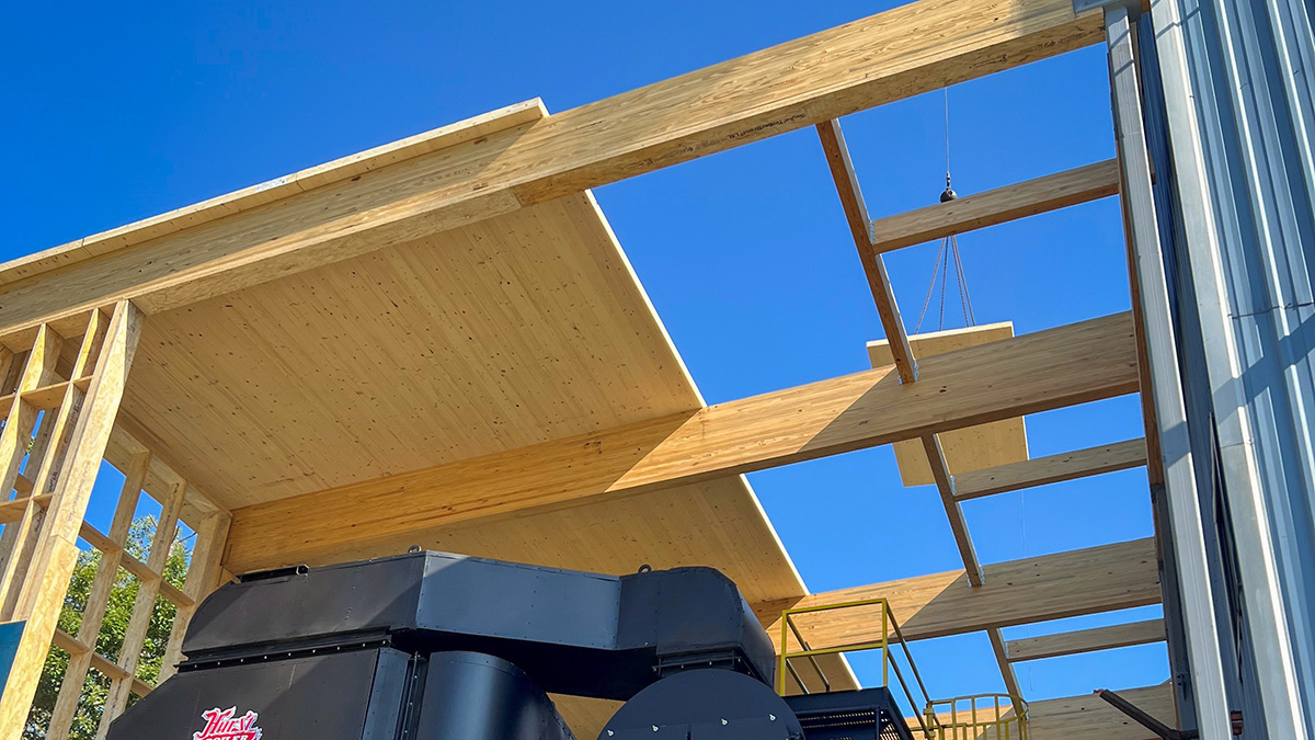 A construction scene of CLT panels being lifted by a crane against a clear blue sky.