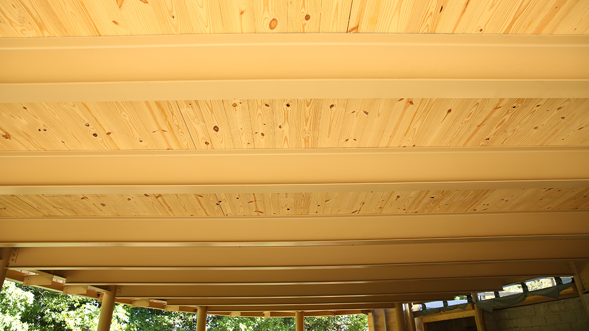 The image shows a wooden ceiling with light-colored steel beams and light-colored wooden planks, likely part of an outdoor structure.