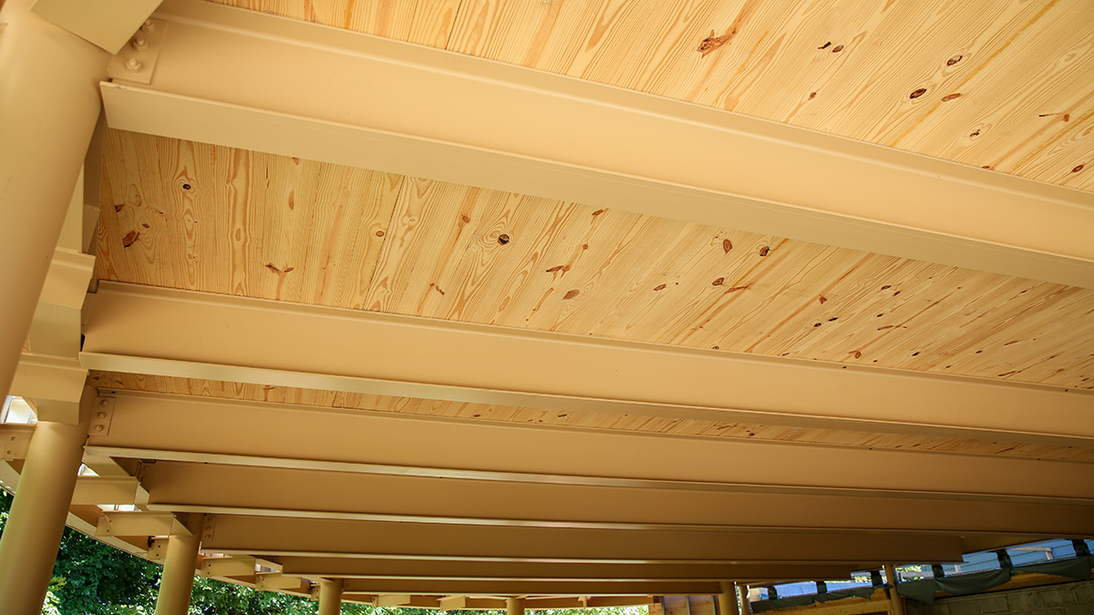 The image shows a wooden ceiling with light-colored steel beams and light-colored wooden planks, likely part of an outdoor structure.