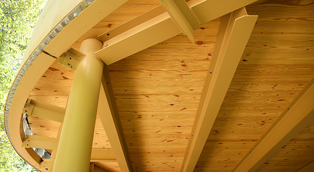 A building under construction with a curved roof, nude colour steel columns, and exposed CLT panels.