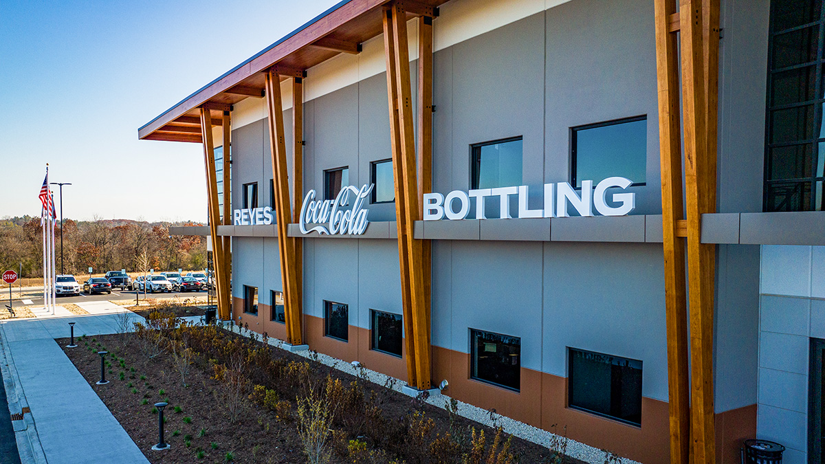 A building facade with signage reading "Reyes Coca-Cola Bottling," featuring wooden beams and windows.