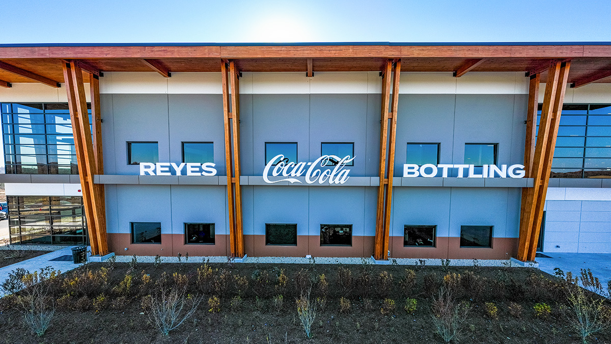 A building facade with signage reading "Reyes Coca-Cola Bottling," featuring wooden beams and windows.