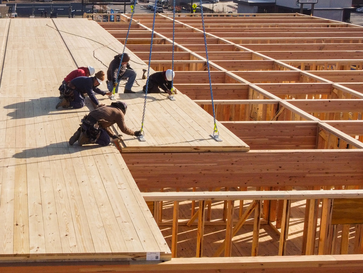 Workers secure mass timber panels onto a building frame with crane assistance.