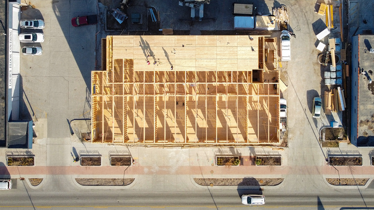 Overhead view of a building under construction with wooden framework and CLT panels, workers visible on-site.