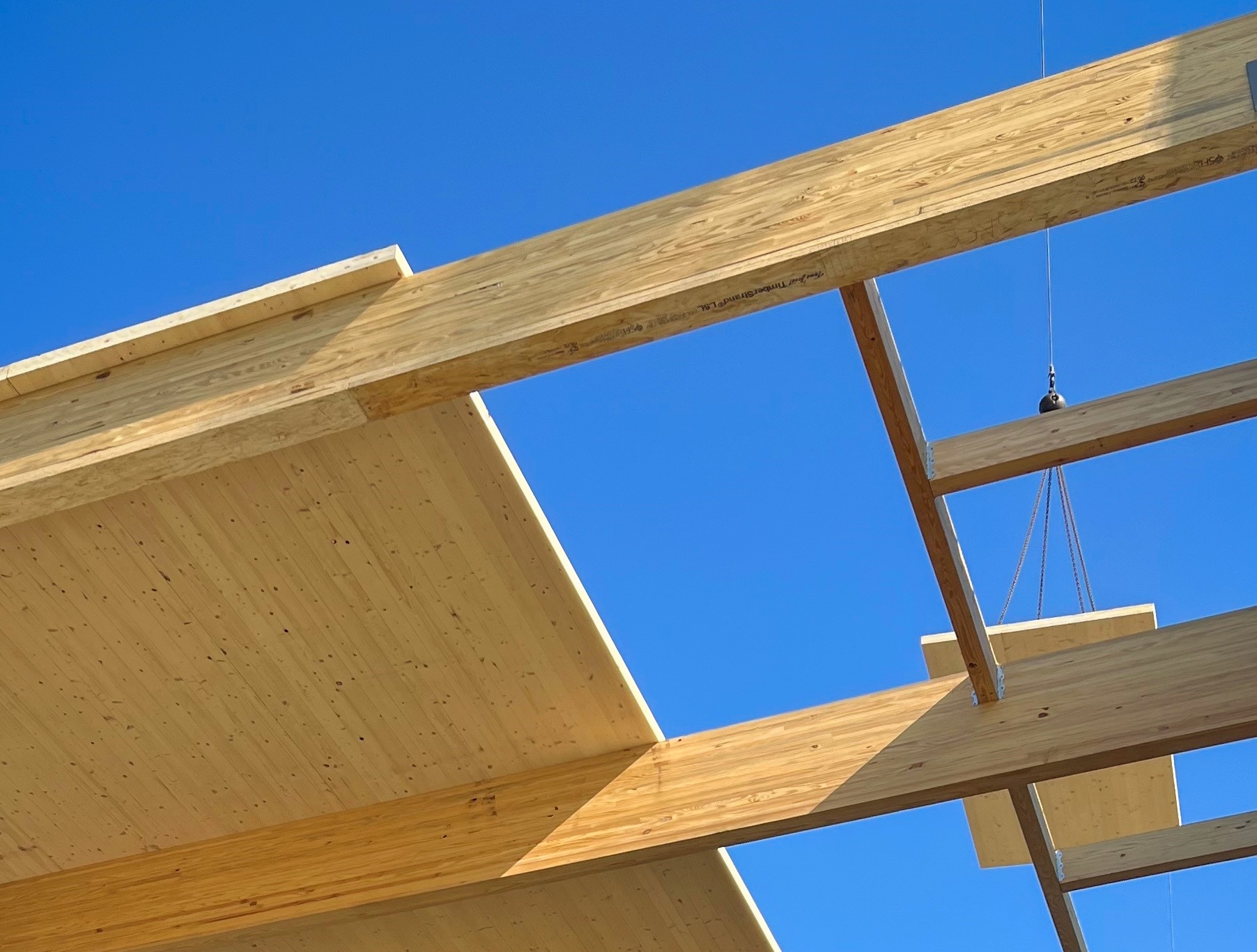 A construction scene of CLT panels being lifted by a crane against a clear blue sky.